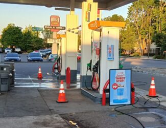 Blocking off lanes with cones "Freshly pressure washed gas station with clean concrete surfaces around fuel pumps, traffic cones for safety, and a Circle K convenience store sign visible at sunset."